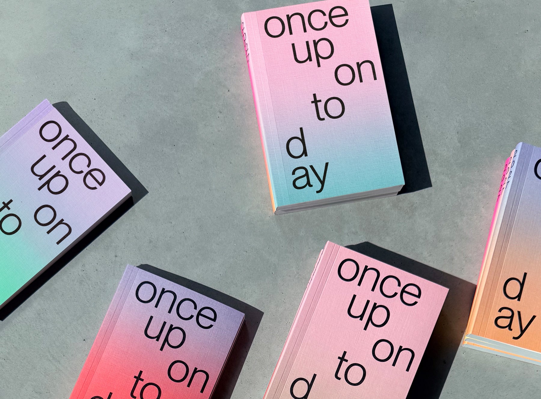 Several stacks of edition julie joliat planner 2027 with black text reading 'once upon today' on the top cover, photographed on a concrete surface in dramatic sunlight and shadow.