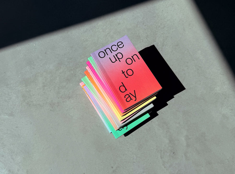 A stack of edition julie joliat planner agenda 2027 with black text reading 'once upon today' arranged on a gray surface under direct sunlight, casting a sharp shadow.