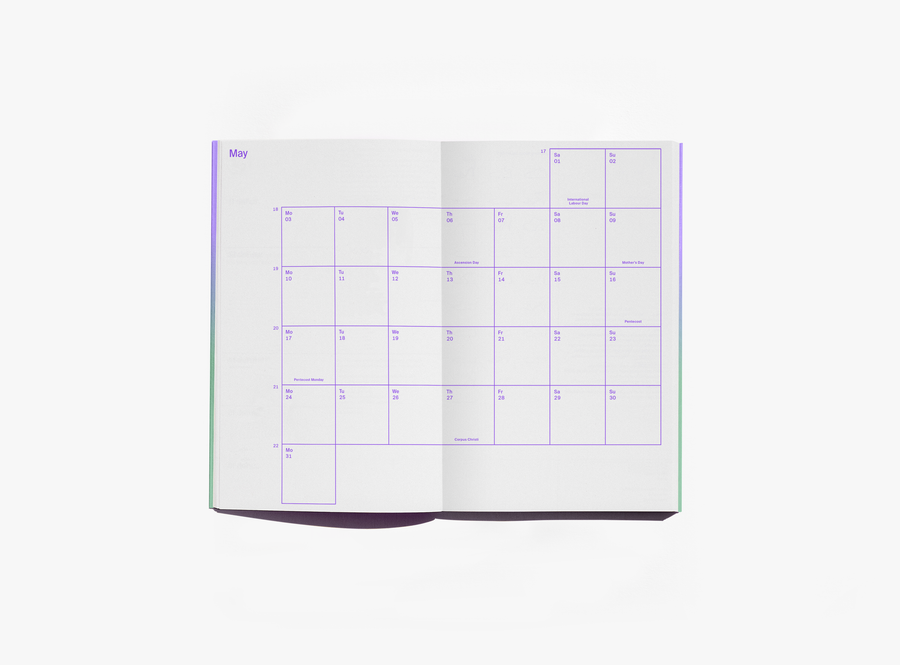 An open edition julie joliat planner agenda 2027  or notebook showing the May monthly calendar layout with purple grid lines and text on white pages, photographed against a clean white background.