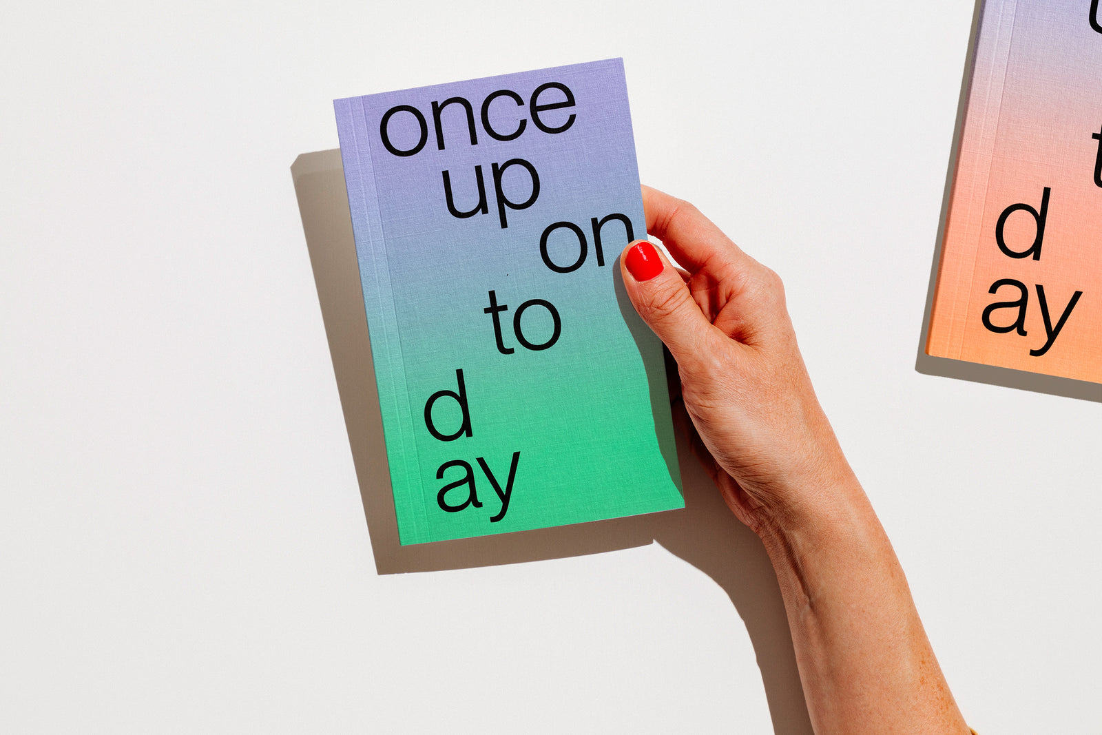 A hand with red nail polish holds a gradient planner 2027 that reads 'once upon today' in black lowercase text against a clean white background. edition julie joliat planner agenda 2027.