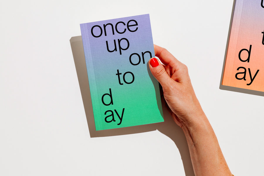 A hand with red nail polish holds a gradient planner 2027 that reads 'once upon today' in black lowercase text against a clean white background. edition julie joliat planner agenda 2027.