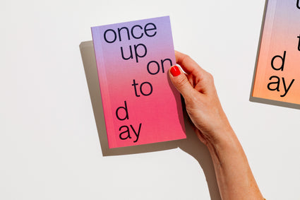 A hand with red nail polish holds a gradient planner 2027 that reads 'once upon today' in black lowercase text against a clean white background. edition julie joliat planner agenda 2027.