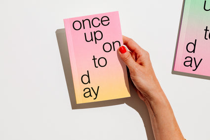 A hand with red nail polish holds a gradient planner 2027 that reads 'once upon today' in black lowercase text against a clean white background. edition julie joliat planner agenda 2027.